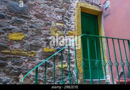 Vecchia porta verde chiusa con cornice gialla in pietra e parete rosa con ringhiera verde in ferro battuto dalla strada. Foto Stock