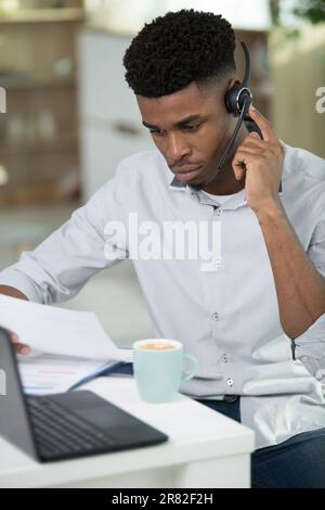 uomo d'affari africano concentrato in cuffie scrivere note in notebook Foto Stock