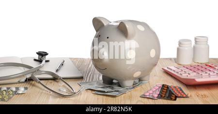 Banco di piggy, stetoscopio, calcolatrice e pillole su tavolo di legno su sfondo bianco. Assicurazione medica Foto Stock