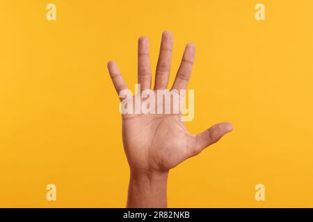 Uomo che dà cinque alti su sfondo giallo, primo piano di mano Foto Stock