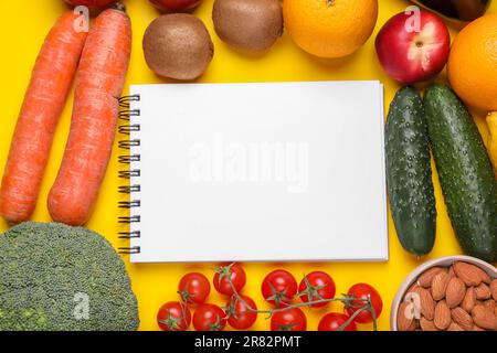 Quaderno, frutta e verdura fresca su sfondo giallo, piatto. Dieta a basso indice glicemico Foto Stock