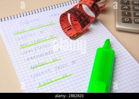 Indice glicemico. Notebook con informazioni, nastro di misurazione, marcatore e calcolatrice su sfondo beige, primo piano Foto Stock
