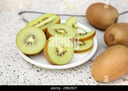 Kiwi interi e tagliati freschi su un tavolo bianco con motivo, primo piano Foto Stock