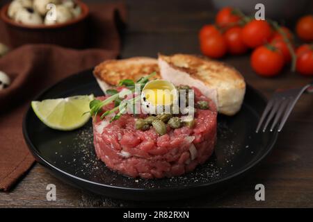 Gustose tartare di bistecca di manzo servite con uova di quaglia e altri accompagnamenti su un tavolo di legno Foto Stock