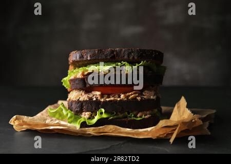 Delizioso panino con tonno, pomodori e lattuga su tavola nera Foto Stock