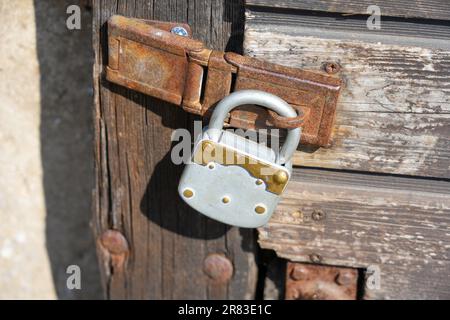 La vecchia serratura è appesa alla porta di legno di un vecchio fienile. Vecchio lucchetto d'epoca. Robusta serratura sul cancello in legno Foto Stock