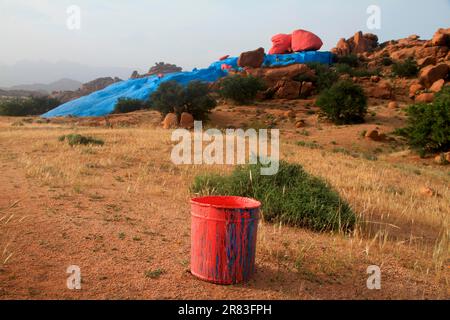 Secchio di vernice vuoto di fronte alle rocce appena dipinte vicino Tafraoute, Antiatlas Marocco Foto Stock