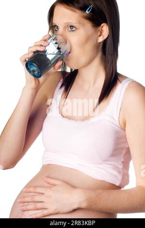 Una ragazza assetata incinta beve acqua da un bicchiere Foto Stock
