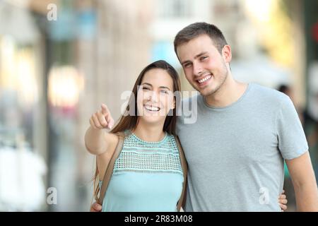 Vista frontale ritratto di una coppia felice che indica qualcosa in strada Foto Stock