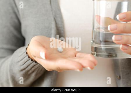 Vista frontale primo piano di una donna che tiene una pillola e un bicchiere d'acqua Foto Stock