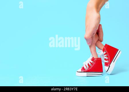 Mano femminile con le dita vestita con scarpe da ginnastica in tela rossa e sistemata in modo da apparire come le gambe su uno sfondo azzurro con spazio copia. Adver creativo Foto Stock