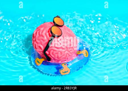 Il personaggio rosa del cervello umano, indossando occhiali da sole alla moda, galleggia senza sforzo in una piscina su un tubo gonfiabile adornato da graziose anatre. Ringiovanimento mentale Foto Stock