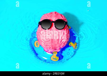 Il personaggio carino, realizzato con un modello cerebrale umano che indossa occhiali da sole, gode di un momento estivo spensierato mentre galleggia su un tubo gonfiabile in acqua. Cre Foto Stock