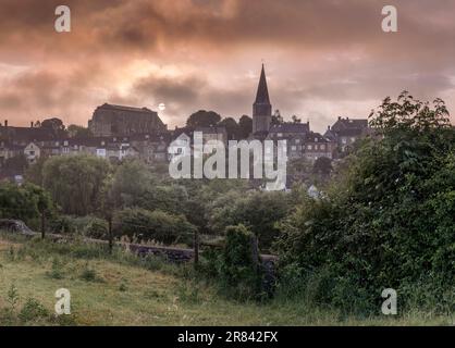 Il sole si mostra attraverso un sottile velo di nuvola bassa mentre sorge sopra la storica abbazia nella città collinare di Malmesbury. Fu fondata la storica abbazia Foto Stock