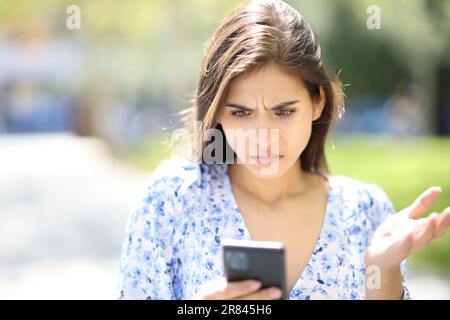 Donna sconvolta che controlla il contenuto del telefono per strada Foto Stock