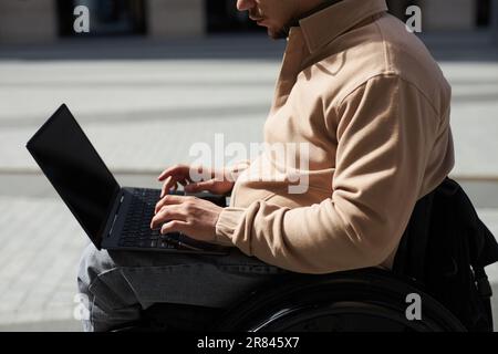 Vista laterale di un giovane con disabilità che lavora a distanza su un computer portatile all'aperto Foto Stock