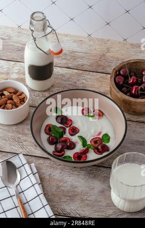 yogurt con ciliegie in un piatto, latte in una bottiglia e bicchiere su un Foto Stock