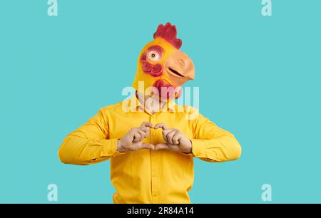 L'uomo divertente con l'umore romantico comico che indossa la maschera di pollo sulla sua testa mostra la forma del cuore. Foto Stock