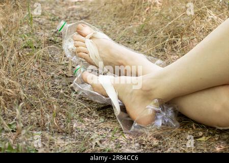 Piedi da donna in scarpe fatte in casa da una bottiglia di plastica nella foresta sulle strade, moda, riutilizzo Foto Stock