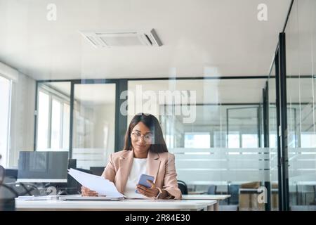 Donna in viaggio d'affari che utilizza dispositivi mobili e lavora con documenti in ufficio. Vista attraverso il vetro Foto Stock