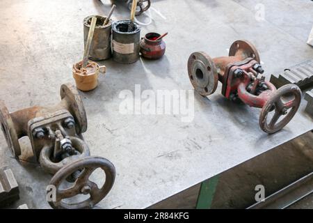 Due chiusure vecchie in metallo, raccordi per tubazioni, lattine con grasso grafite, olio solido in fabbrica, in officina. Foto Stock