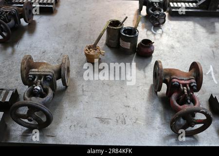 Due chiusure vecchie in metallo, raccordi per tubi, lattine con grasso grafite, solidol su un grande tavolo di ferro in fabbrica, negozio. Foto Stock