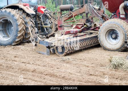 Un trattore con un'unità di semina collegata, una mietitrebbia, una perforatrice con ruote grandi ara il campo, semina prodotti di grano, esegue lavori agricoli e agricoli sul campo Foto Stock