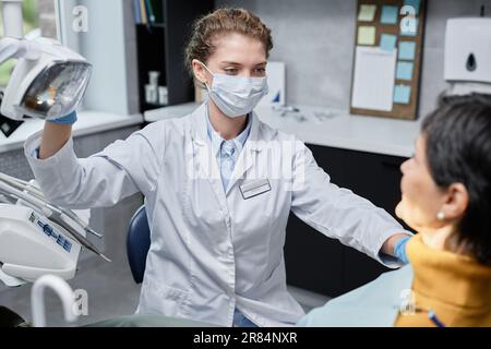 Ritratto di giovane donna come dentista femmina che regola le luci in preparazione per l'esame in clinica dentale Foto Stock