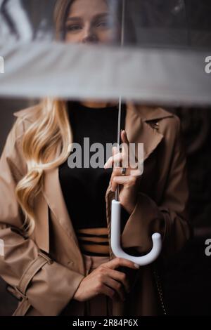 concentratevi sulle mani che tengono l'ombrello trasparente nelle giornate di pioggia. donna guarda la macchina fotografica attraverso un ombrello trasparente Foto Stock