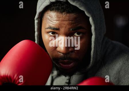 Primo piano del giovane pugile afro-americano maschio concentrandosi sul prossimo calcio mentre in piedi di fronte al sacchetto di punzonatura e andando a colpirlo Foto Stock