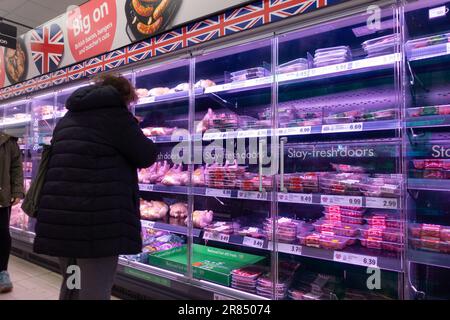 Donna in giacca nera invernale che guarda la navata della carne a Lidl, ashford, kent, uk Foto Stock