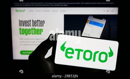 Persona che tiene uno smartphone con il logo della società israeliana di commercio sociale eToro sullo schermo di fronte al sito web. Messa a fuoco sul display del telefono. Foto Stock