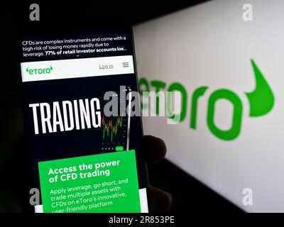 Persona che tiene uno smartphone con una pagina web della società israeliana di social trading eToro sullo schermo di fronte al logo. Messa a fuoco al centro del display del telefono. Foto Stock