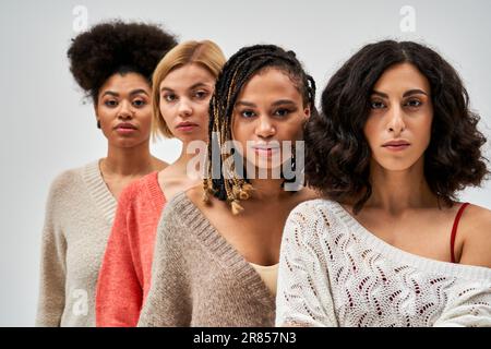 Ritratto di donne multietniche in elegante caldo maglioni guardando la macchina fotografica vicino a fiends sfocati isolati sul grigio, diversi tipi di corpo e auto-accettanc Foto Stock