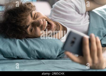 Buon uomo arabo videochiamare una ragazza su uno smartphone sul letto dopo il risveglio al mattino Foto Stock