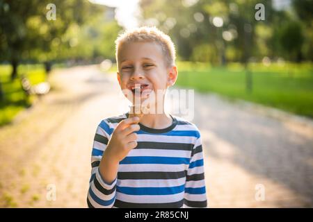 Ritratto di ragazzo felice che sta in piedi nel parco e mangiare gelato. Foto Stock