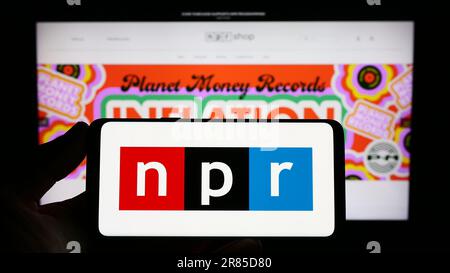 Persona che tiene uno smartphone con il logo dell'organizzazione dei media National Public radio (NPR) sullo schermo di fronte al sito Web. Messa a fuoco sul display del telefono. Foto Stock