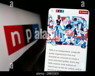 Persona che tiene il cellulare con il sito web di organizzazione di media National Public radio (NPR) sullo schermo con il logo. Messa a fuoco al centro del display del telefono. Foto Stock