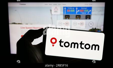 Persona che tiene il cellulare con il logo della società olandese di tecnologia di localizzazione TomTom NV sullo schermo di fronte alla pagina web aziendale. Messa a fuoco sul display del telefono. Foto Stock