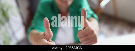Donna di affari riuscita che mostra i pollici in su sul posto di lavoro nell'ufficio Foto Stock