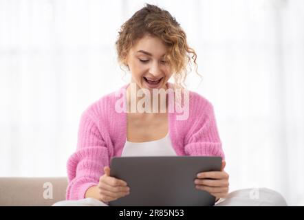 Vincita online. Donna gioiosa che guarda lo schermo del notebook a casa con entusiasmo Foto Stock