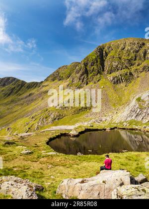 Un escursionista a Hard Tarn sotto Nethermost Pike sulla catena Helvellyn, Lake District, Regno Unito. Foto Stock