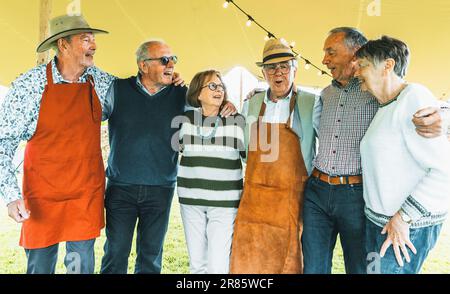 Diversi gruppi di anziani che hanno una gioiosa festa all'aperto in campagna, abbracciando, ridendo, e festeggiando insieme. Foto Stock