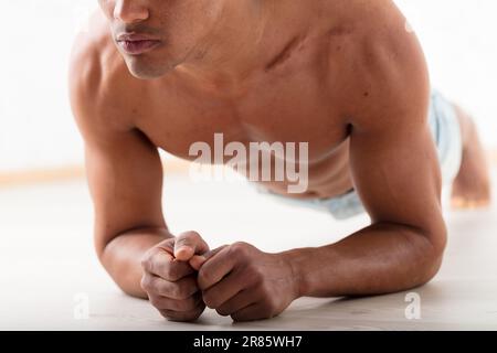 Un uomo nero non identificabile esegue una tavola con i gomiti a terra. I suoi percettibili Pecs e abs dimostrano che l'esercizio migliora l'appeal e la salute Foto Stock