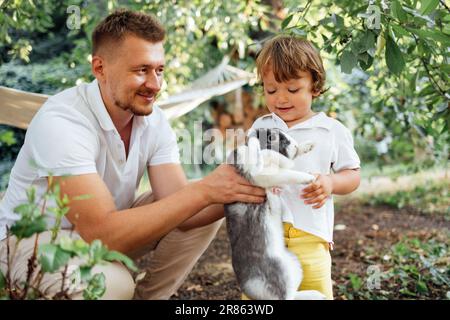 Un giovane sorride e tiene un coniglio nana carino nelle sue mani all'aperto. Il bambino dolce è felice e tocca un animale domestico soffice. Un uomo attraente mostra un Foto Stock