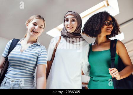 Gli studenti delle scuole superiori carini in un college o in un edificio universitario. Belle amici multirazziali femmina sorridere e andare a studiare. Ragazze attraenti con backp Foto Stock