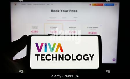Persona che tiene uno smartphone con il logo della conferenza francese Viva Technology (VivaTech) sullo schermo di fronte al sito Web. Messa a fuoco sul display del telefono. Foto Stock