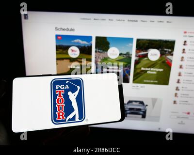 Persona che tiene il cellulare con il logo dell'organizzazione di golf degli Stati Uniti PGA Tour sullo schermo di fronte alla pagina web. Messa a fuoco sul display del telefono. Foto Stock