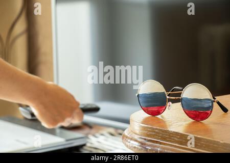 La bandiera della Russia sugli occhiali che giacciono sul tavolo a casa sullo sfondo della TV, la Russia e la propaganda dalla TV, si trova e inganno Foto Stock