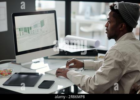 Giovane uomo nero in casualwear che guarda gli schizzi grafici sullo schermo del computer mentre crea disegni per un nuovo progetto architettonico Foto Stock